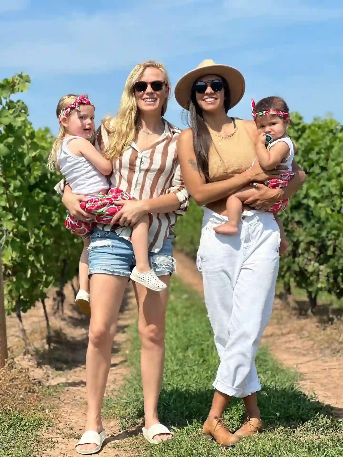 Morgan and Ale walking through a sunlit vineyard with their daughters
